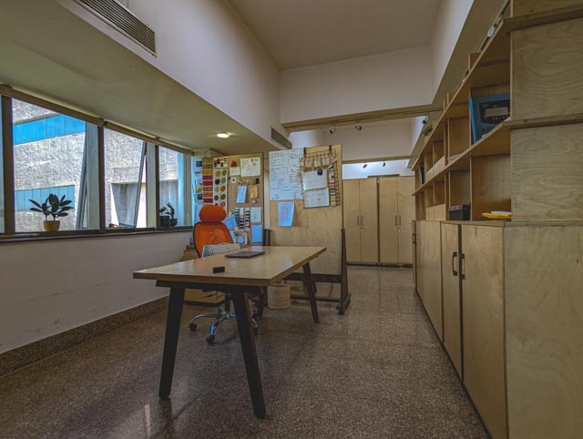 Studio Atmosphere: Natural light from the large side windows illuminates the workspace, highlighting the textures of the materials and the terrazzo flooring.