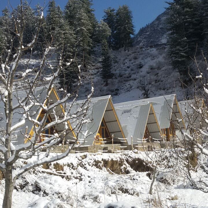 Alpine geometry: A series of A-frame cabins designed with steep sloping roofs to shed snow, sitting harmoniously within the frozen landscape.