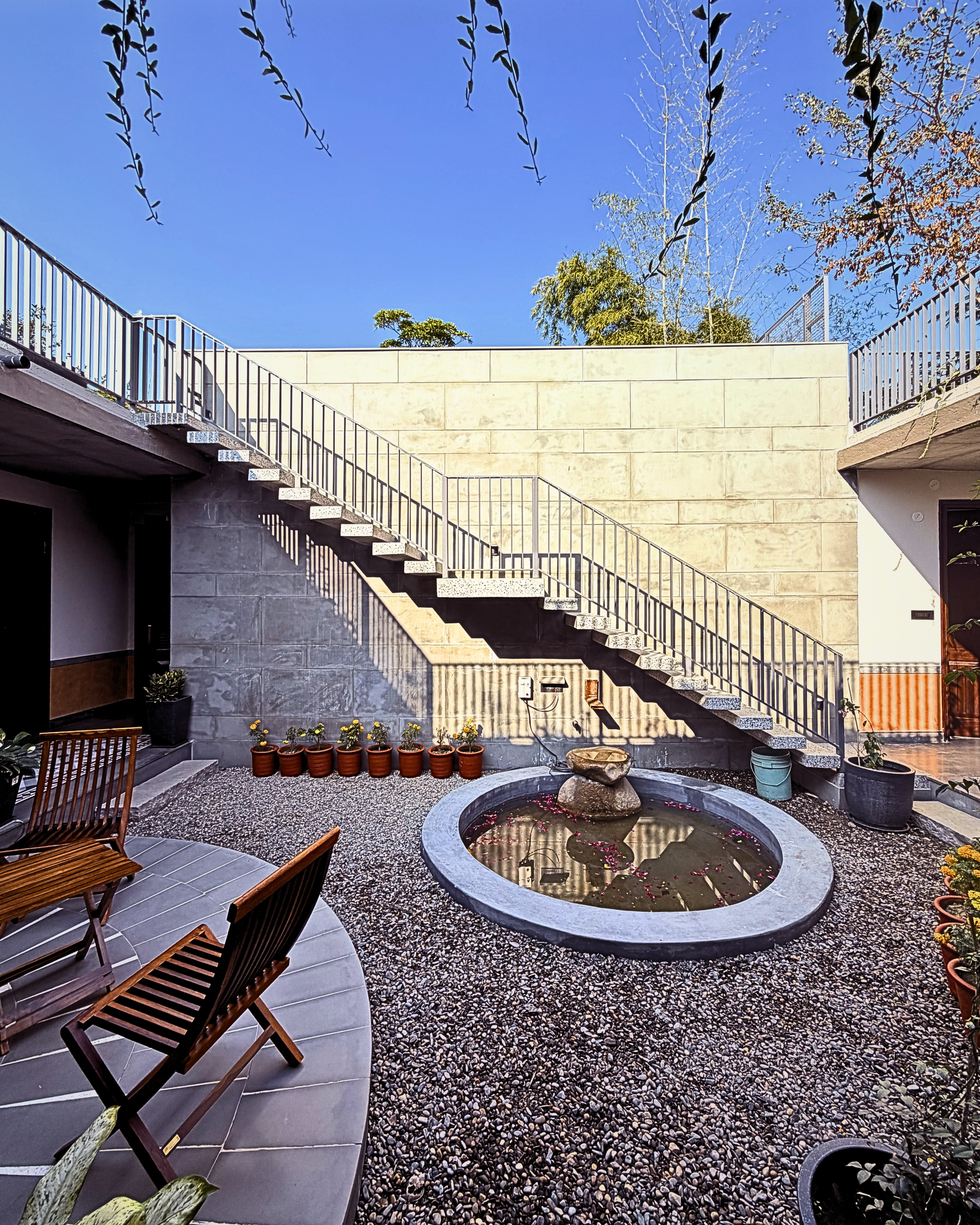 Connecting spaces: The open-riser staircase adds a sense of lightness to the textured walls, linking the patio to the upper terrace while casting intricate shadows on the sunlit wall.