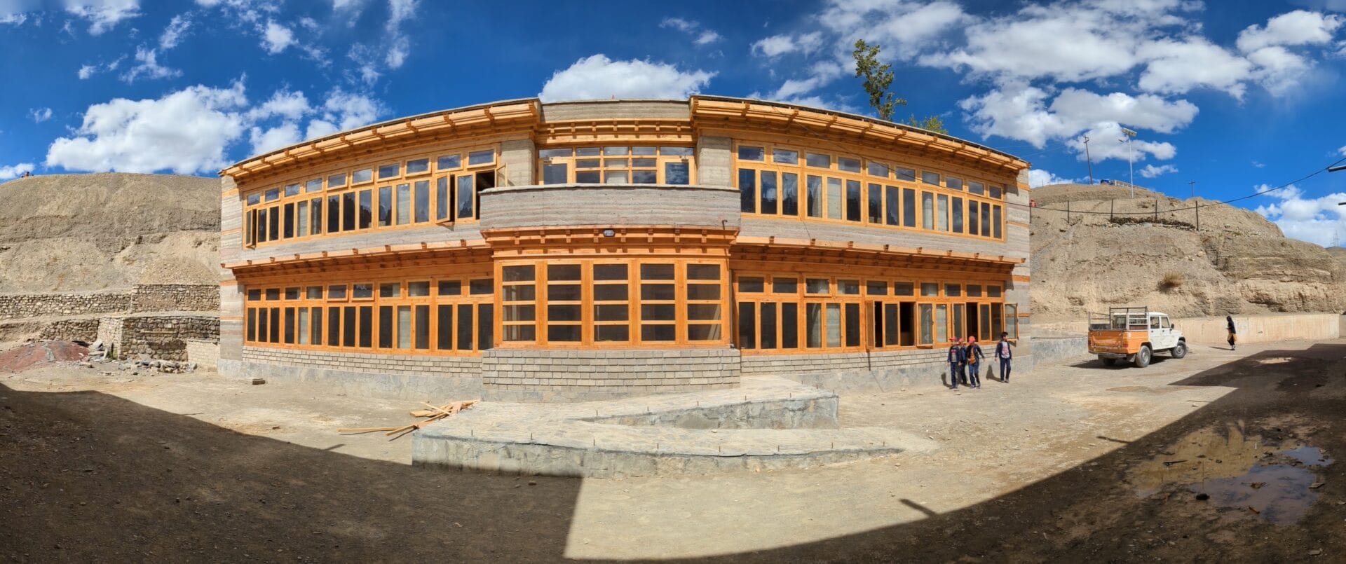 Earth and Sky: This panoramic view captures the sweeping facade of the school, showcasing the rich texture of the rammed earth walls and the rhythmic grid of wooden windows.