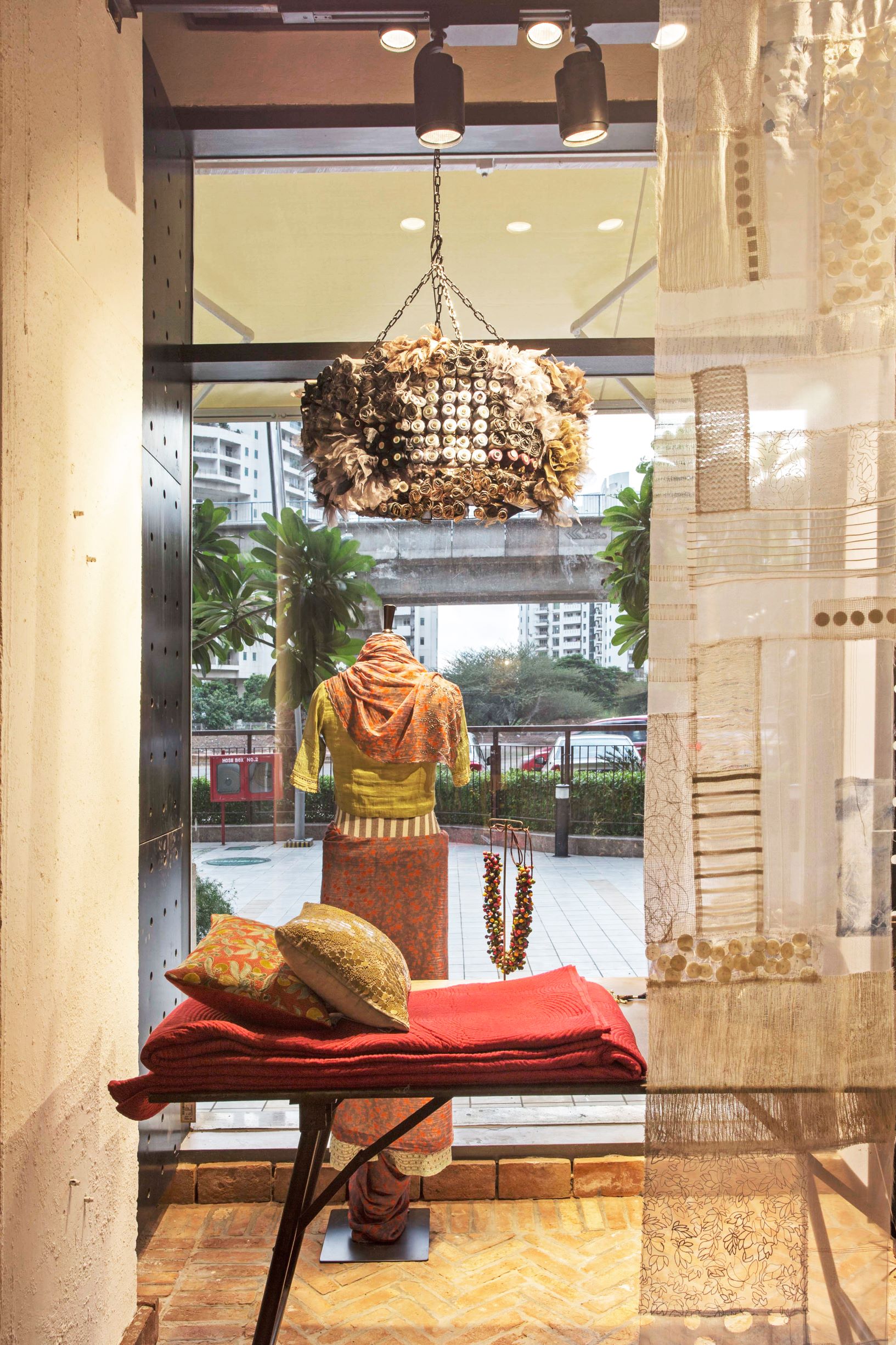 A layered view: The shop window features a curated mix of fashion and decor, highlighted by a statement light fixture and warm brick flooring.