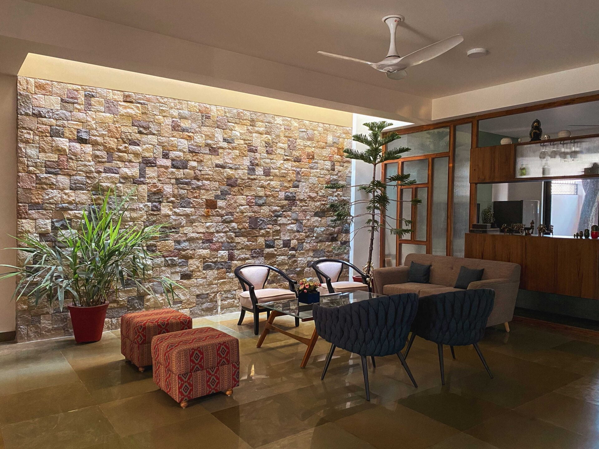 A refined indoor lounge featuring a textured stone feature wall, polished flooring, curated seating, warm ambient lighting, and indoor greenery creating a calm, composed atmosphere.