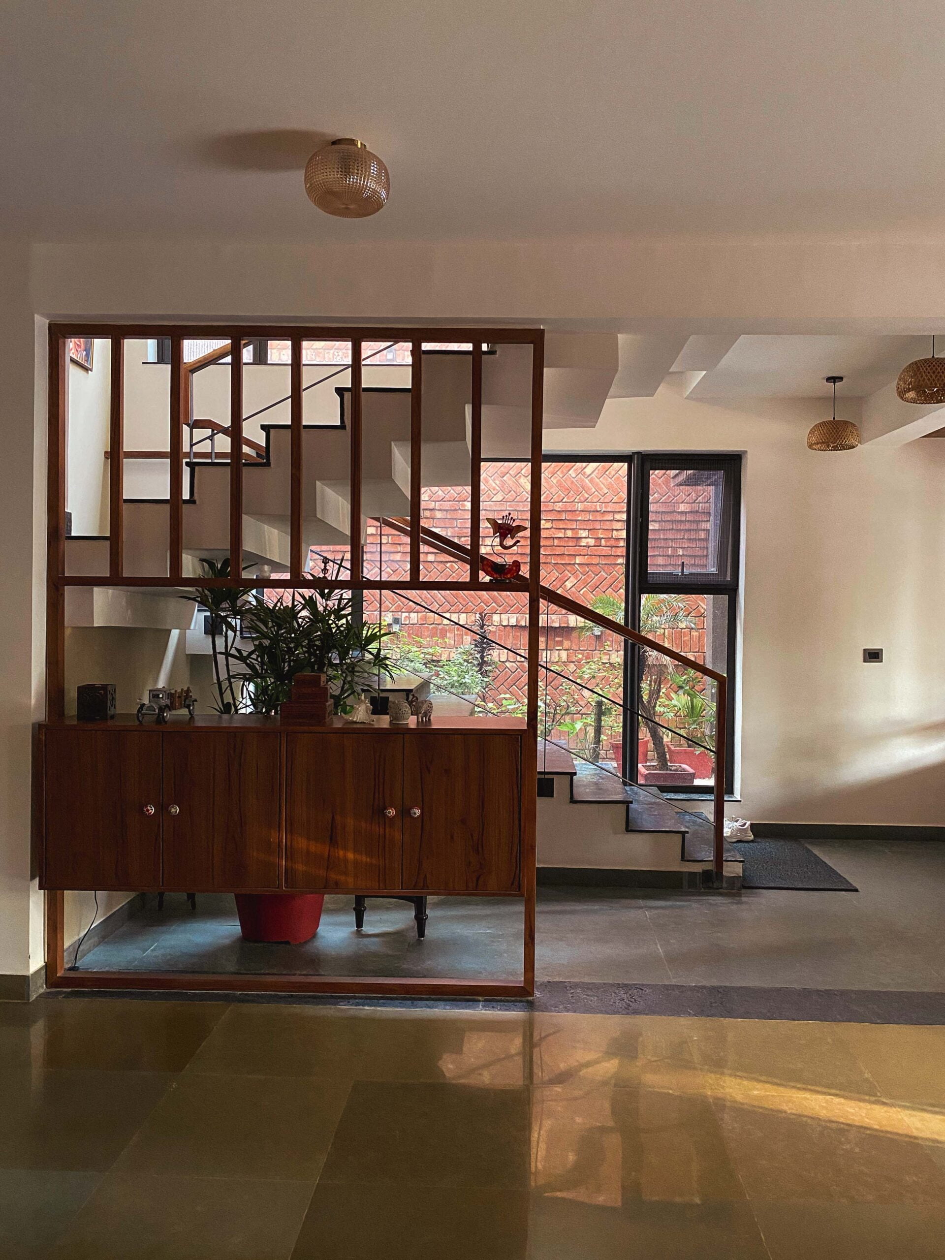 A warm, moder.n interior with a white staircase framed by wooden partitions, natural light, indoor plants, and subtle mid-century detailing