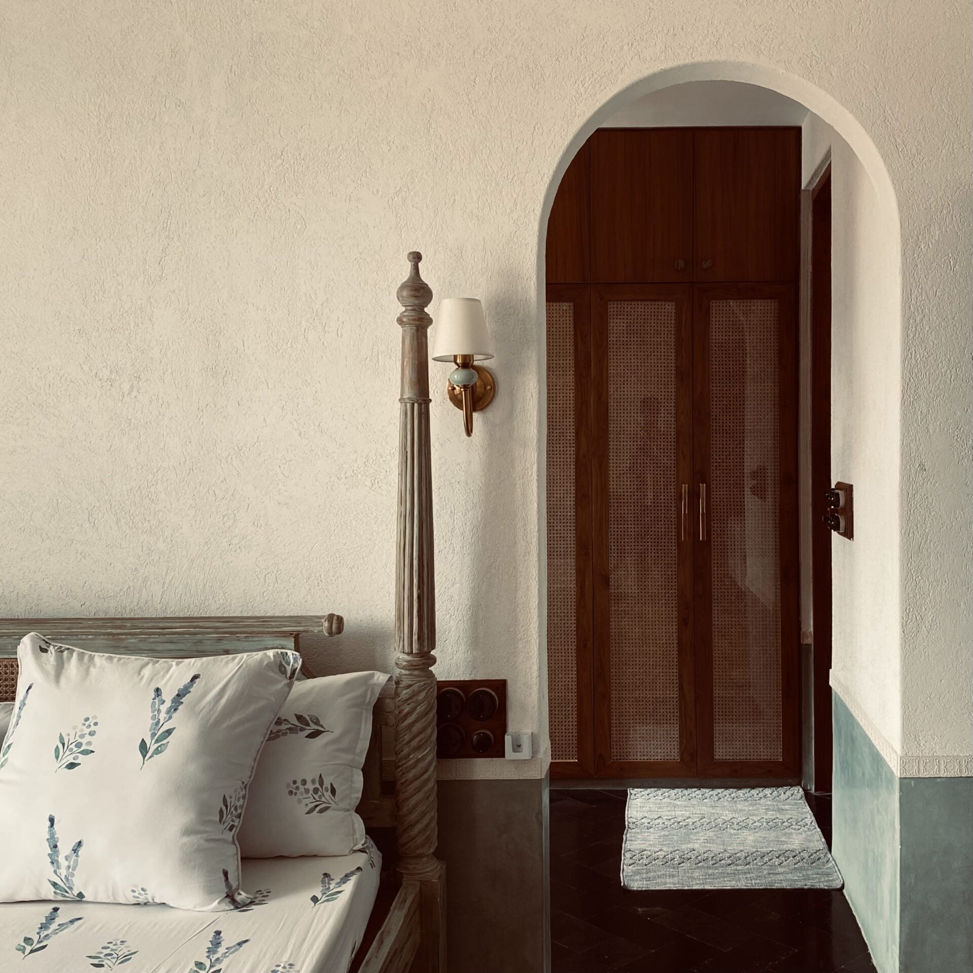 Old-world charm: A distressed four-poster bed and a graceful arched doorway framing the rattan wardrobe create a serene, vintage-inspired retreat.